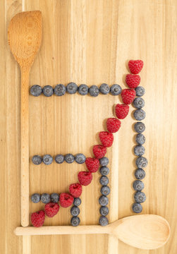 Statistical line curve graph made of kitchen spoons, fresh blueberries and raspberries on a brown wooden cutting board