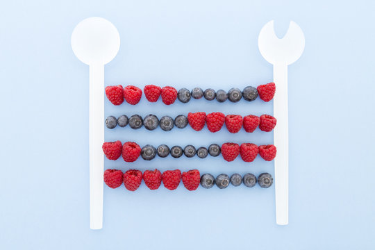 Vintage abacus calculator frame made of kitchen spoons, fresh blueberries and raspberries on a pale blue paper background