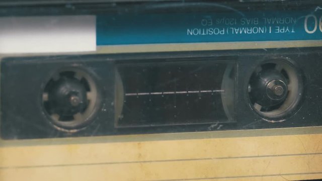 The Vintage Audio Cassette in the Tape Recorder Rotates. Macro static camera view of a vintage audio cassette tape with a blank label in use sound recording in a cassette player.