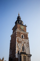 Upper part of the town hall clock tower in Krakow with half moon in the evening sky and birds flying.