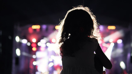 Little girl on her father’s shoulder watching and cheering in the audience during concert. Public concert, no ticketing event