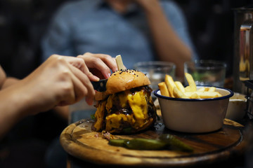 Homemade double cheese burger meat with pickle cucumber and french fries on wood plate. Delicious menu in rustic restaurant. Women hand cutting cheese burger.