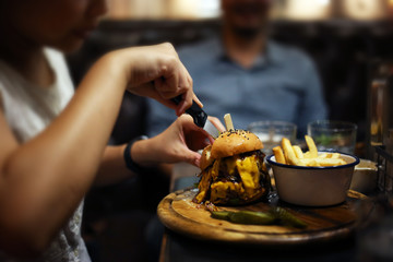 Homemade double cheese burger meat with pickle cucumber and french fries on wood plate. Delicious menu in rustic restaurant. Women hand cutting cheese burger.