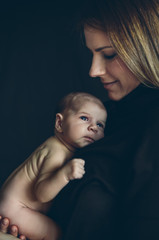 Nude baby girl posing in her mother's arms on black background