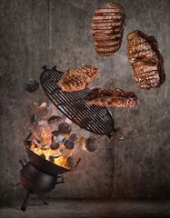 Foto op Canvas Kettle grill with hot briquettes, cast iron grate and tasty beef steaks flying in the air. High resolution image. © Lukas Gojda