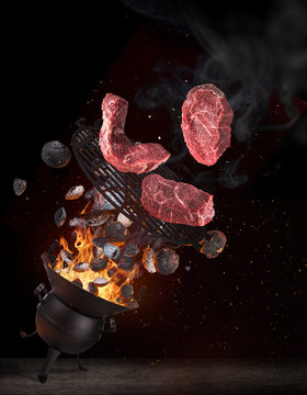 Kettle grill with hot briquettes, cast iron grate and tasty beef steaks flying in the air. High resolution image.