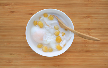Thai dessert, Ball flour with poached egg in sweet coconut milk in white bowl against wooden background.