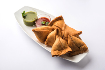 Veg Samosa is a triangle shape pakora stuffed with Aloo sabji, served with green chutney and tomato sauce. selective focus
