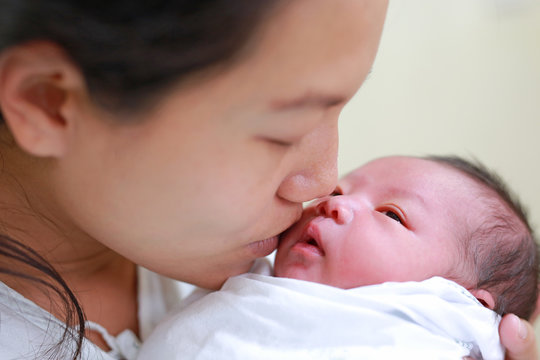 Closeup mother kissing infant baby in her arms in hospital after delivery room.
