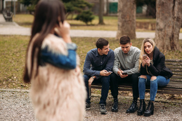 Young people having a good time in park. Male and female sitting on the bench and using phones