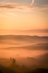 Obraz premium Picturesque sunrise in Tuscany, Italy. Misty morning with light fog shapes magically the hills and valleys of this beautiful tourist location in San Quirico d'Orcia region. Vertical image