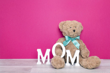 Toy bear with letters MOM on fuchsia background.
