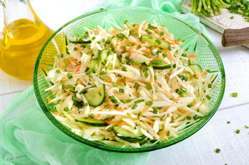 Dietary salad with cabbage, cucumber, carrot, greens. Juicy spring salad from fresh vegetables on a white wooden background. Proper nutrition.