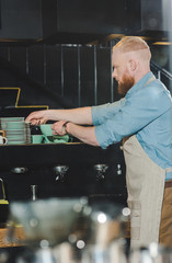 side view of young male barista taking saucer for coffee mug