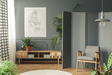 Retro armchair against a gray screen next to a drawing hanging on a dark wall with molding above...