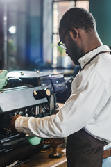 side view of young african american barista in eyeglasses working with coffee machine in coffee shop