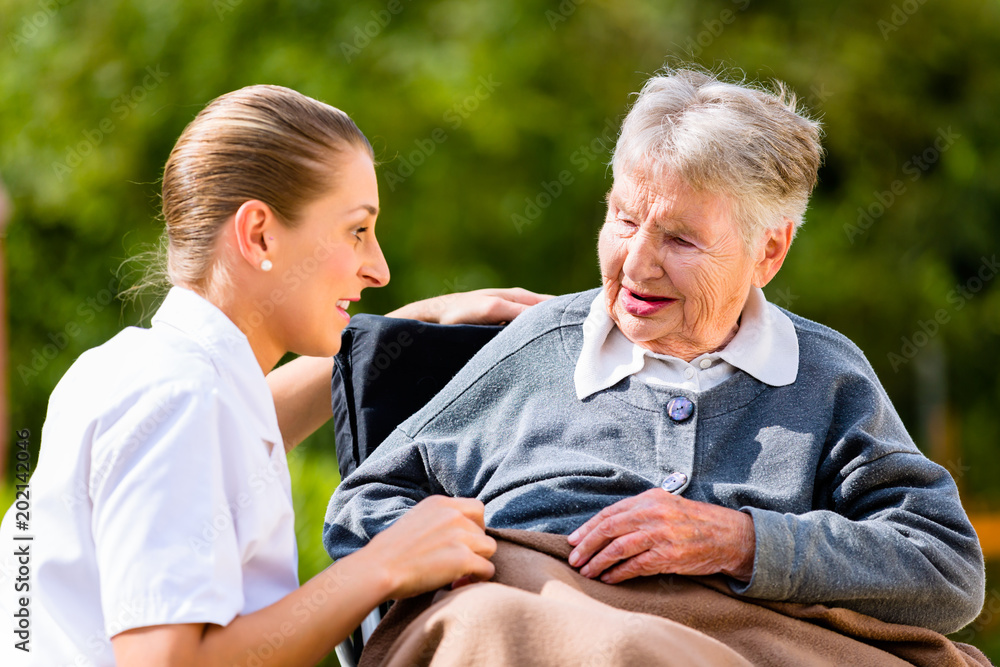 Sticker nurse holding hands with senior woman sitting in wheelchair in garden of retirement home