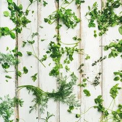 Flat-lay of various fresh green herbs. Parsley, mint, dill, cilantro, rosemary, thyme over white wooden background, top view, square crop. Healthy vegan cooking concept