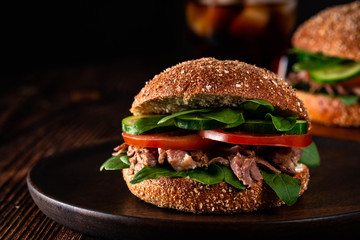 Cheese burger with grilled meat, cheese, tomato, cucumber, spinach on dark wooden surface. Ideal for advertisement. Close-up