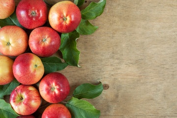 a lot of red ripe apples with green leaves on a wooden background