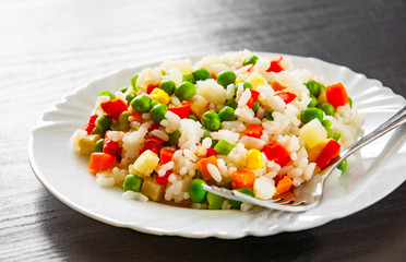 Rice with mixed vegetables on white plate. on dark wooden table
