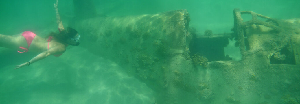 UNDERWATER: Young female traveler explores sunken airplane while diving in ocean
