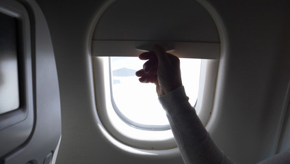 Fototapeta na wymiar CLOSE UP: Unknown person pulls up airplane window shade and reveals blue sky.