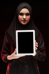 Portrait of beautiful smart young muslim woman wearing black hijab holding tablet in her hands as education concept on black background