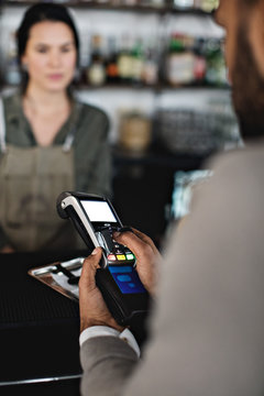 Customer using credit card reader to pay female waiter at checkout counter