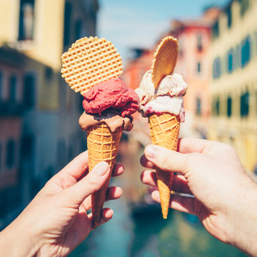 Woman's and man's hands holding italian ice cream in waffle cone on summer light.