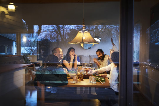 Multi-generation family talking while having dinner at table seen through window