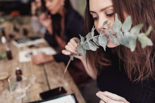 Woman smelling leaves while sitting at table in perfume workshop