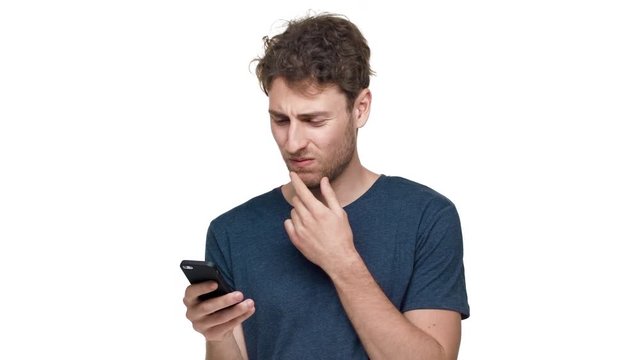 Portrait of young pleased man having bristle using smartphone and scrolling news feed, isolated over white background in studio closeup. Concept of emotions