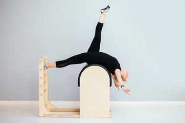 Beautiful blond curly woman in black sportswear performing pilates exercise, training on barrel...