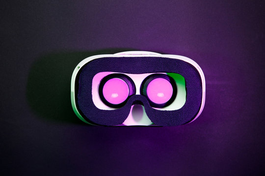 Photo of virtual reality glasses with burning pink light on black background