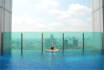 A man from back looking at amazing view of Bangkok from turqouise swimming pool