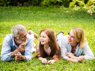 Fototapeta premium Happy family having fun together in the garden. Father, mother and daughter laying down on grass in a park.