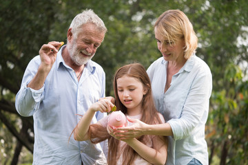 Father, mother and daughter holding a piggy bank and coins in a park. Family and saving for future concept.