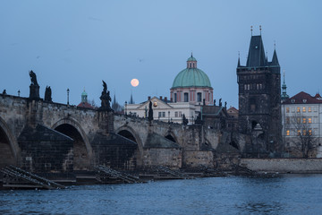 Fototapeta na wymiar The moon rises over the famous Charles bridge in Prague old town in Czech Republic capital city during twilight