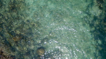 Aerial: overhead  view of transparent green foaming  waves against the rocky line and bottom