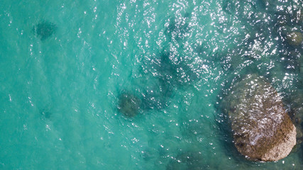 Aerial: overhead  view of transparent green foaming  waves against the rocky line and bottom