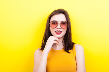 Fototapeta premium Sexy woman wearing sunglasses smiling to the camera on yellow background