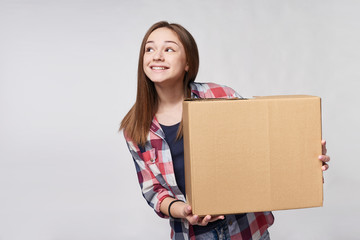 Delivery, relocation and unpacking. Smiling young woman holding cardboard box, looking at blank...