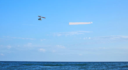 Fototapeta na wymiar Advertising airplane carryng banner with advertising along crowdy beach