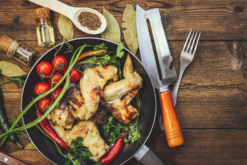 cooking fried chicken wings in a frying pan. spices and vegetables. old kitchen accessories. wooden background