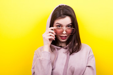 Sexy woman wearing a hood and eyeglasses on yellow background