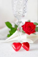 Wedding or Valentine's Day concept. Two red heart, champagne glass and red rose on white concrete table
