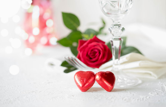 Wedding or Valentine's Day concept. Two red heart, champagne glass and red rose on white concrete table