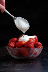 Strawberry in plate with sour cream on black background