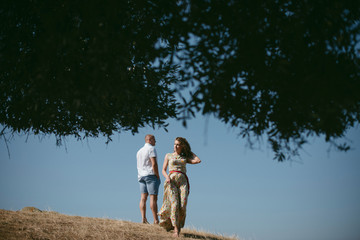 Young couple in love standing on the top of the hill. Woman walking away from man. Sunny day. Greece